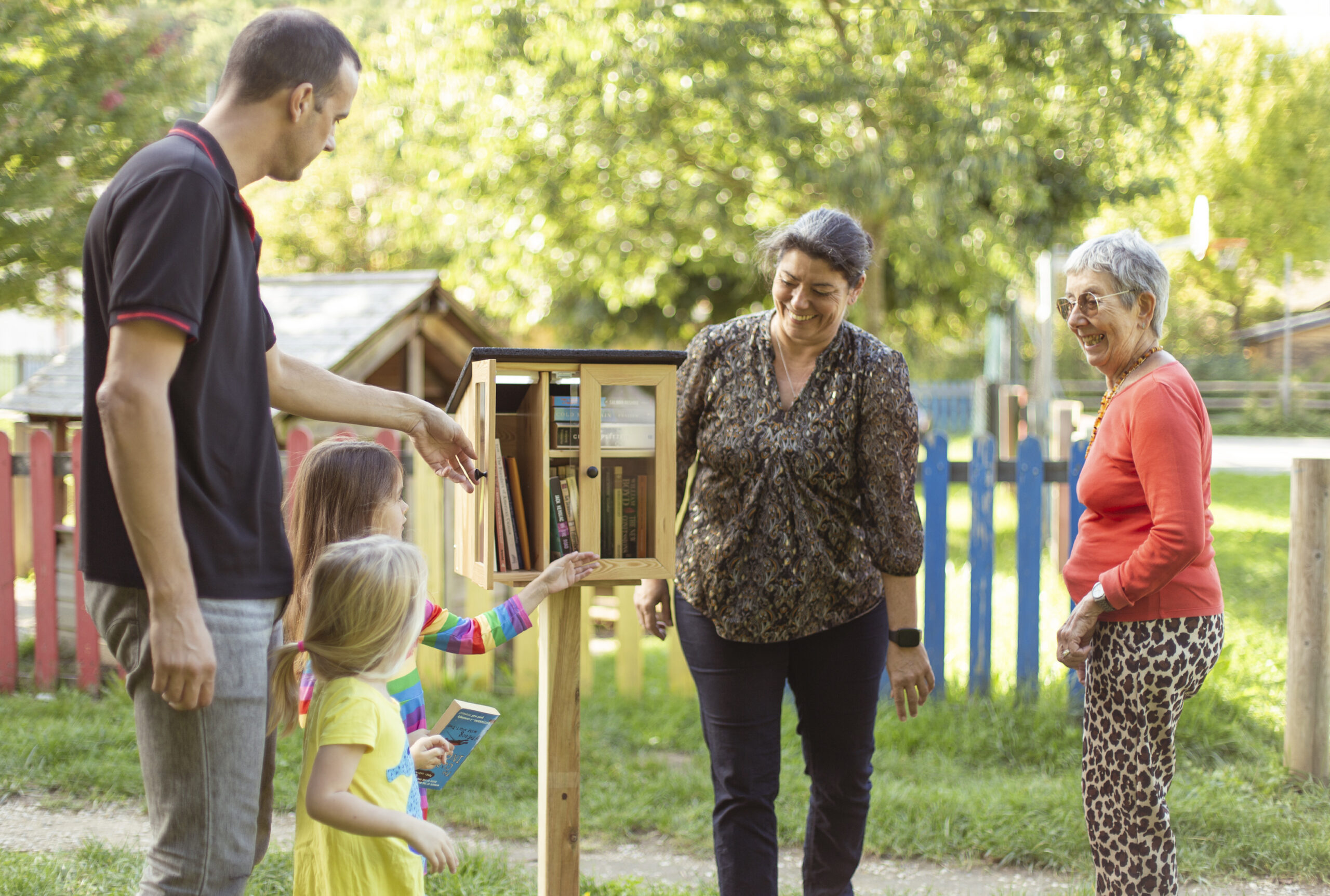 Children and adults sharing books around a wooden outdoor library.